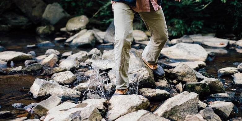 Man walking on rocks in the middle of a stream collecting eDNA samples to use with a water filter.